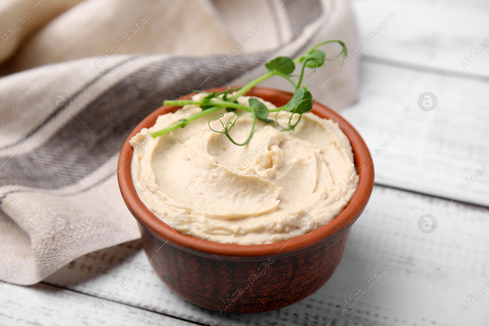 Photo of Bowl with delicious hummus on white wooden table, closeup