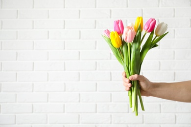 Man holding bouquet of beautiful spring tulips near brick wall, closeup with space for text. International Women's Day