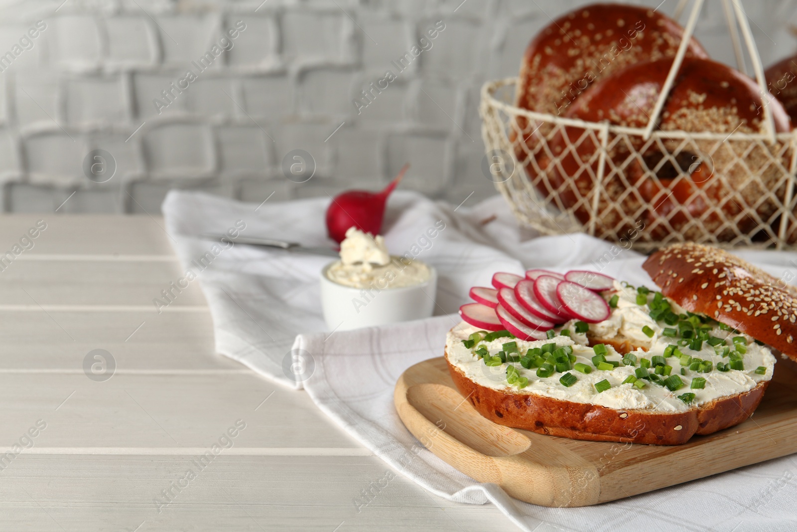Photo of Delicious bagel with cream cheese, radish and green onion on white wooden table. Space for text