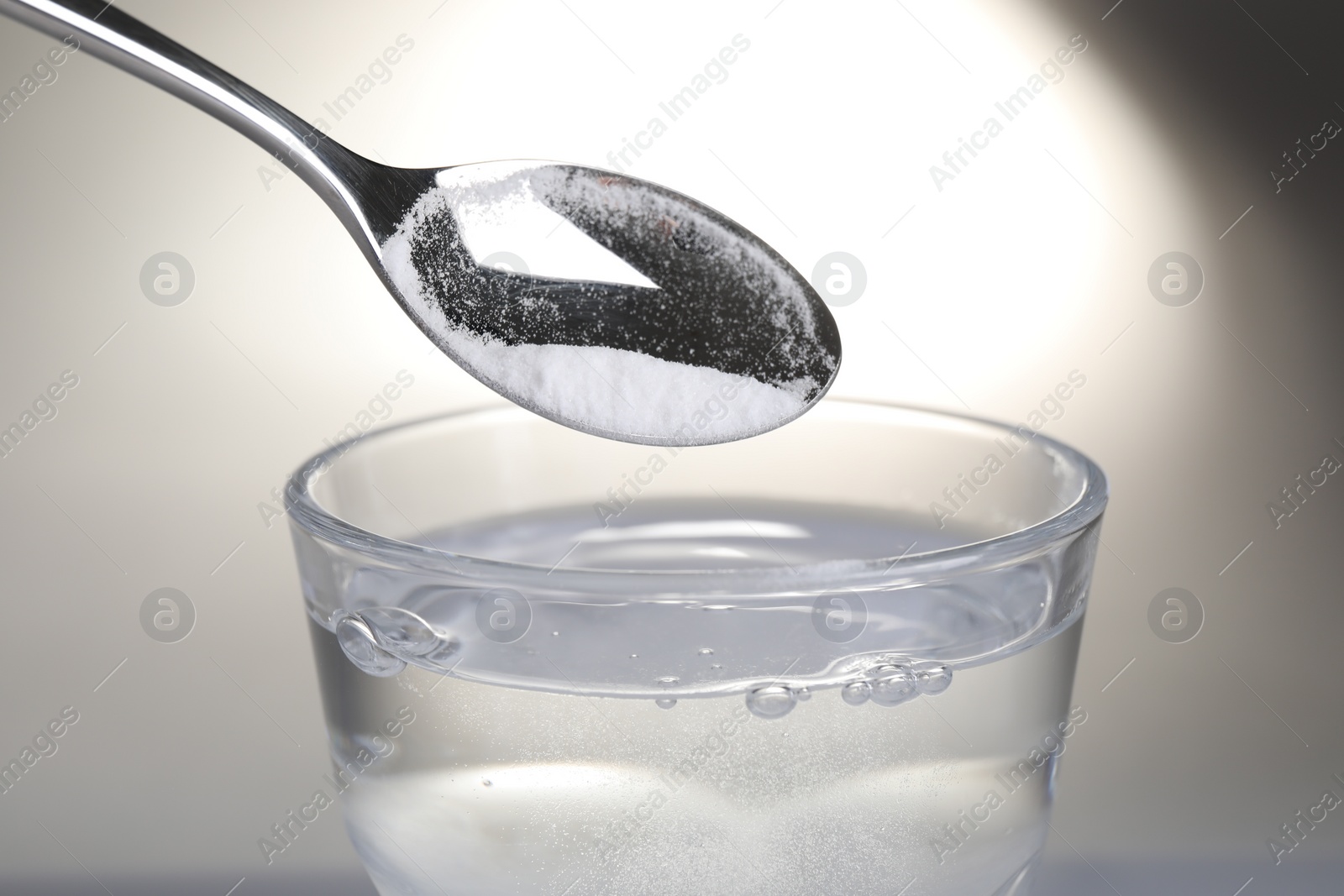 Photo of Adding baking soda into glass of water on light background, closeup