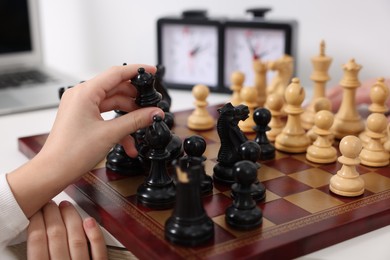 Little child playing chess at table indoors, closeup