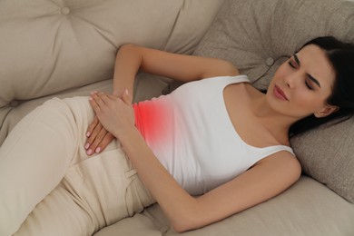 Image of Woman suffering from appendicitis inflammation on sofa indoors