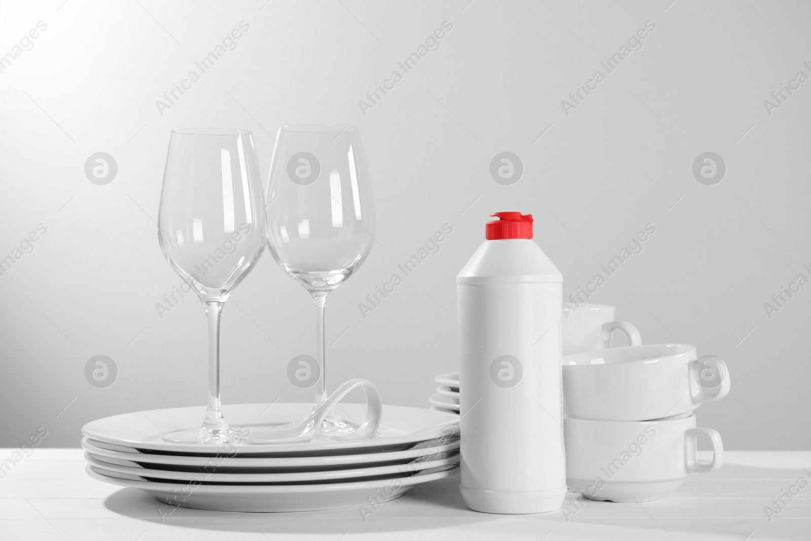 Photo of Set of clean tableware, glasses and dish detergent on white wooden table against light background