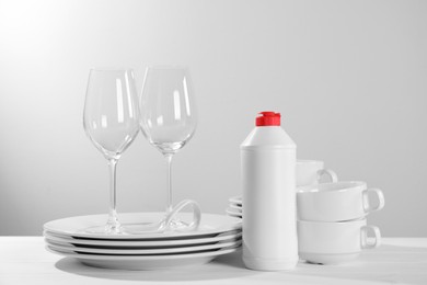 Photo of Setclean tableware, glasses and dish detergent on white wooden table against light background
