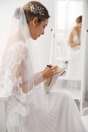 Photo of Young bride writing her single friends names on shoe indoors. Wedding superstition