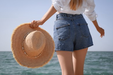 Young woman with straw hat near sea on sunny day in summer, closeup back view