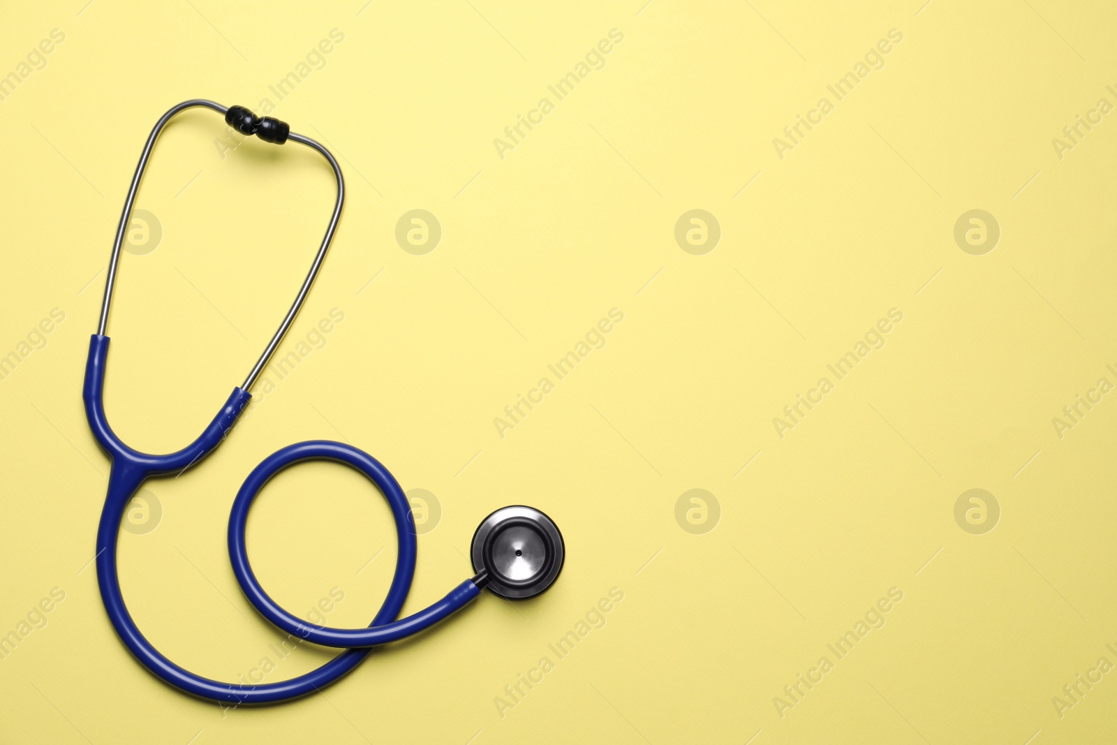 Photo of Stethoscope on yellow background, top view. Space for text