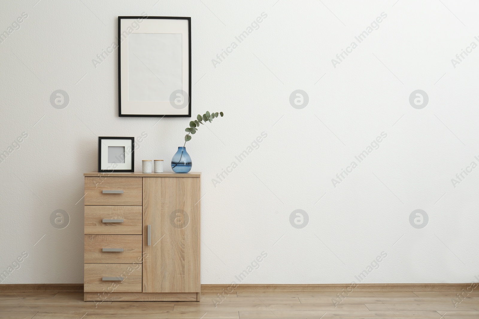 Photo of Wooden cabinet and photo frames in room with white wall, space for text. Interior design