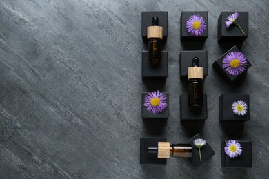 Photo of Flat lay composition with bottles of essential oil and beautiful flowers on dark gray stone table. Space for text