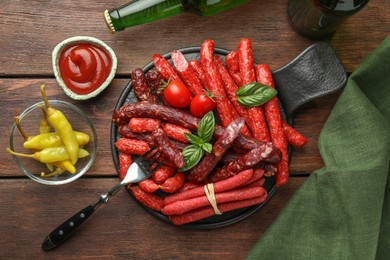 Different thin dry smoked sausages, sauce and tomatoes on wooden table, flat lay