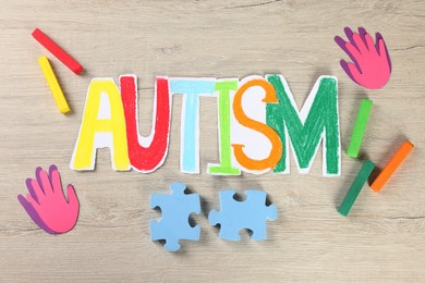 Photo of Word Autism made of paper, puzzle pieces and crayons on white wooden table, flat lay