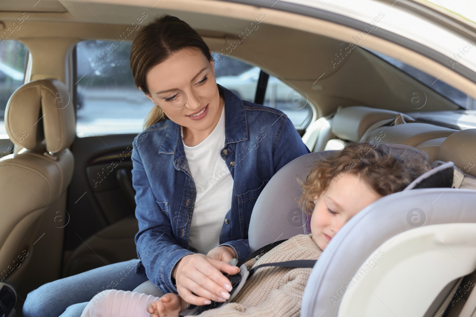 Photo of Mother fastening her sleeping daughter in child safety seat inside car