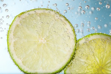 Photo of Juicy lime slices in soda water against light blue background, closeup