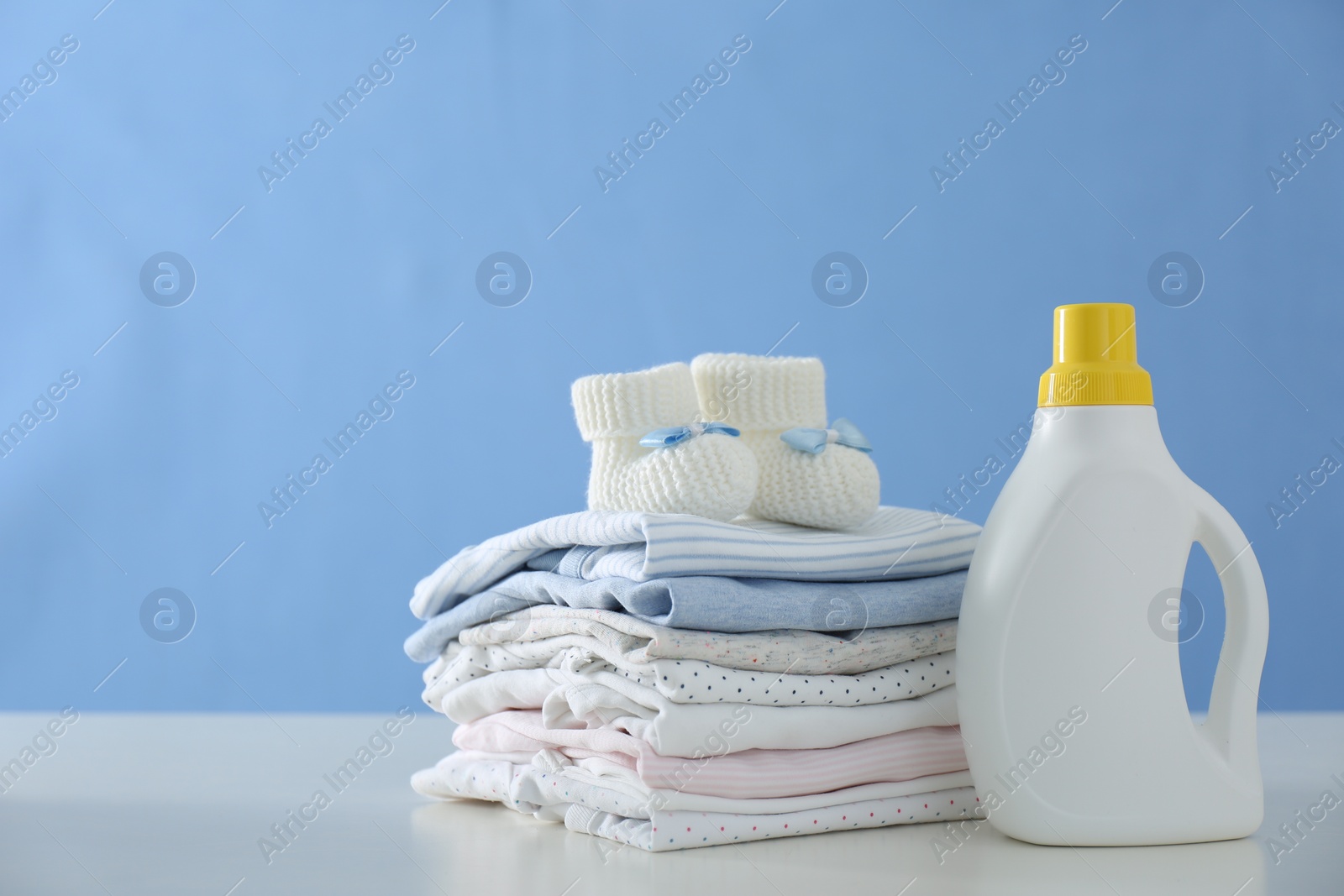 Photo of Detergent and children's clothes on white table near blue wall