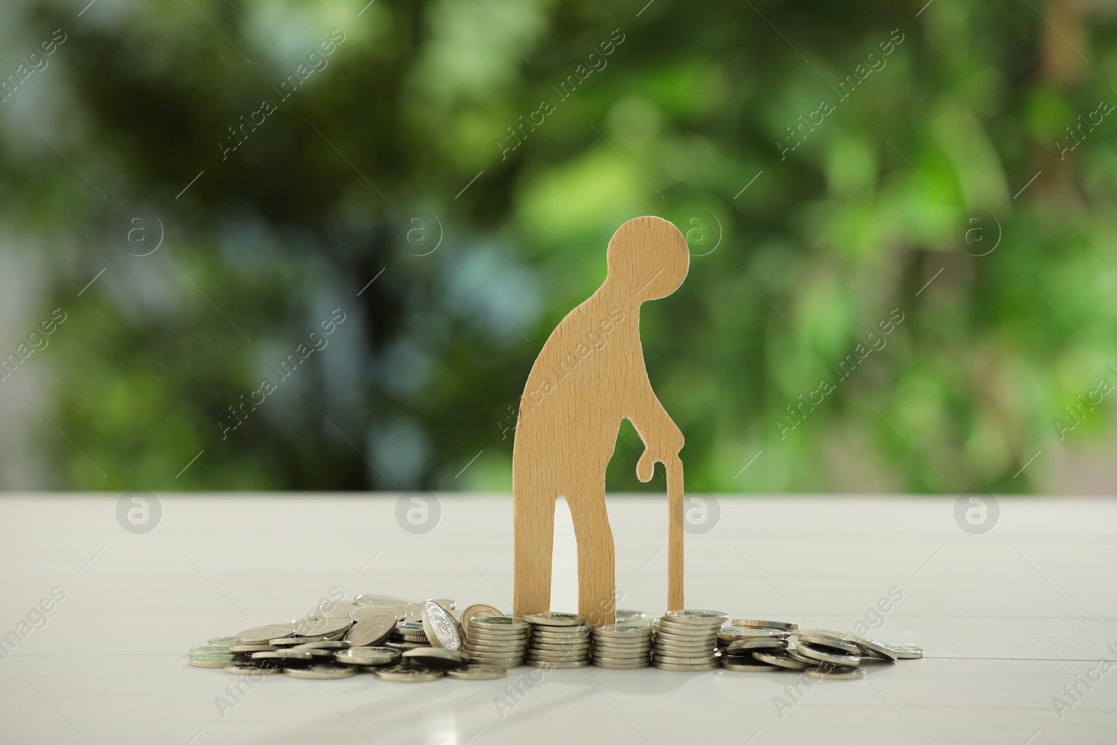 Photo of Pension savings. Figure of senior man and coins on white table against blurred green background