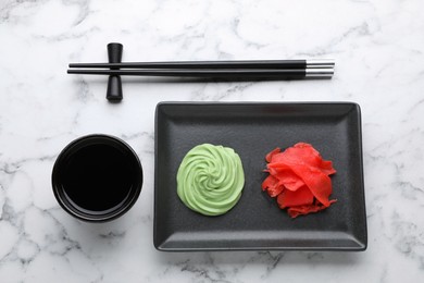 Photo of Swirl of wasabi paste, pickled ginger, soy sauce and chopsticks on white marble table, flat lay