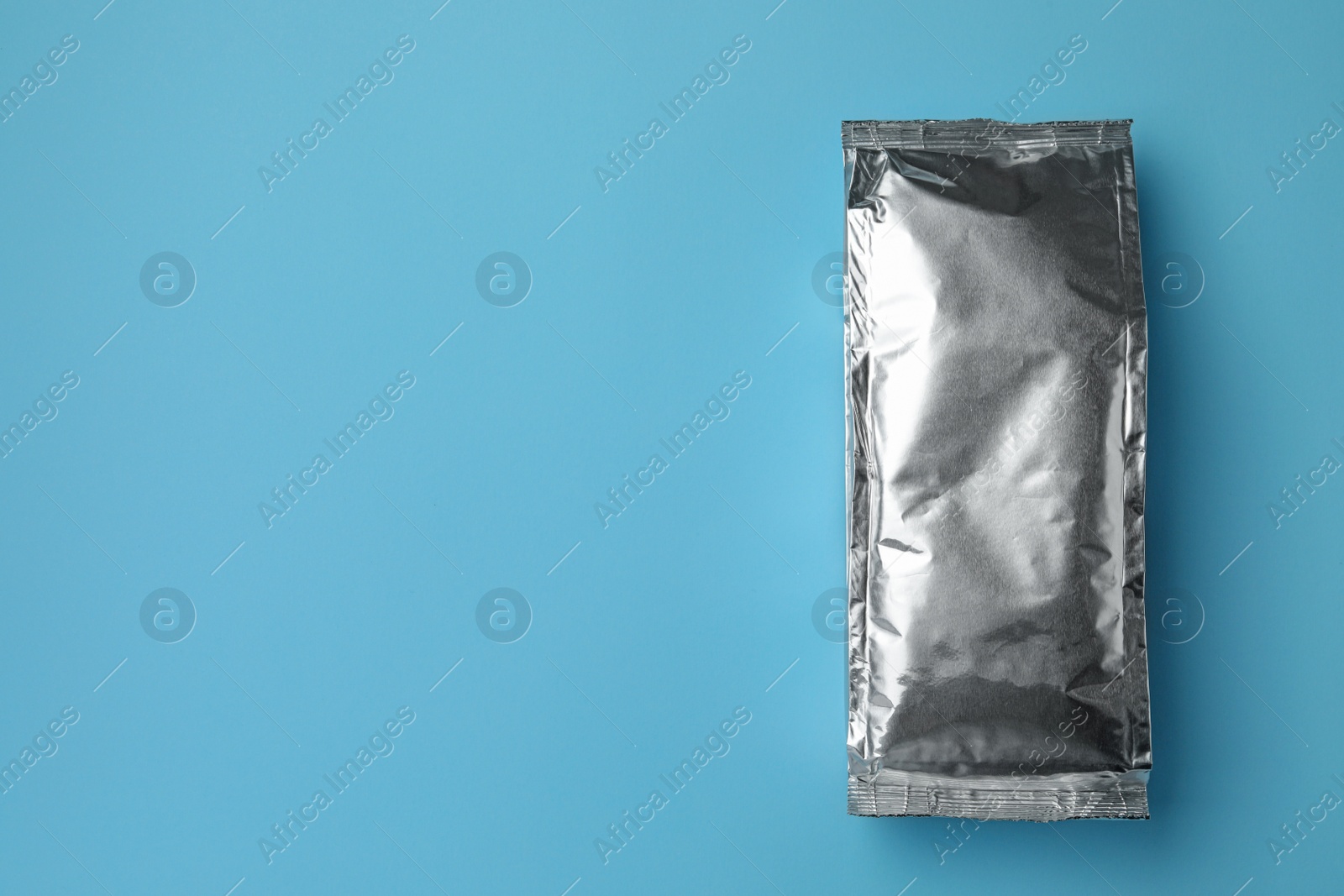 Photo of Blank foil package on light blue background, top view. Space for text