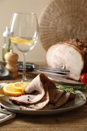 Photo of Slices of delicious baked ham, orange, rosemary and glass with drink on wooden table