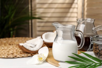 Photo of Glass jug of delicious vegan milk near coconuts on white table indoors. Space for text