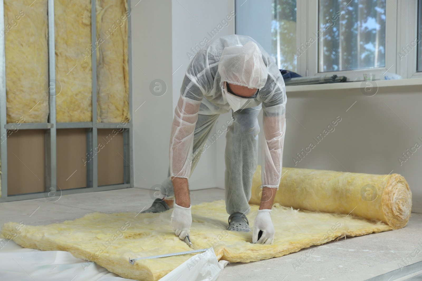 Photo of Worker measuring and cutting insulation material indoors