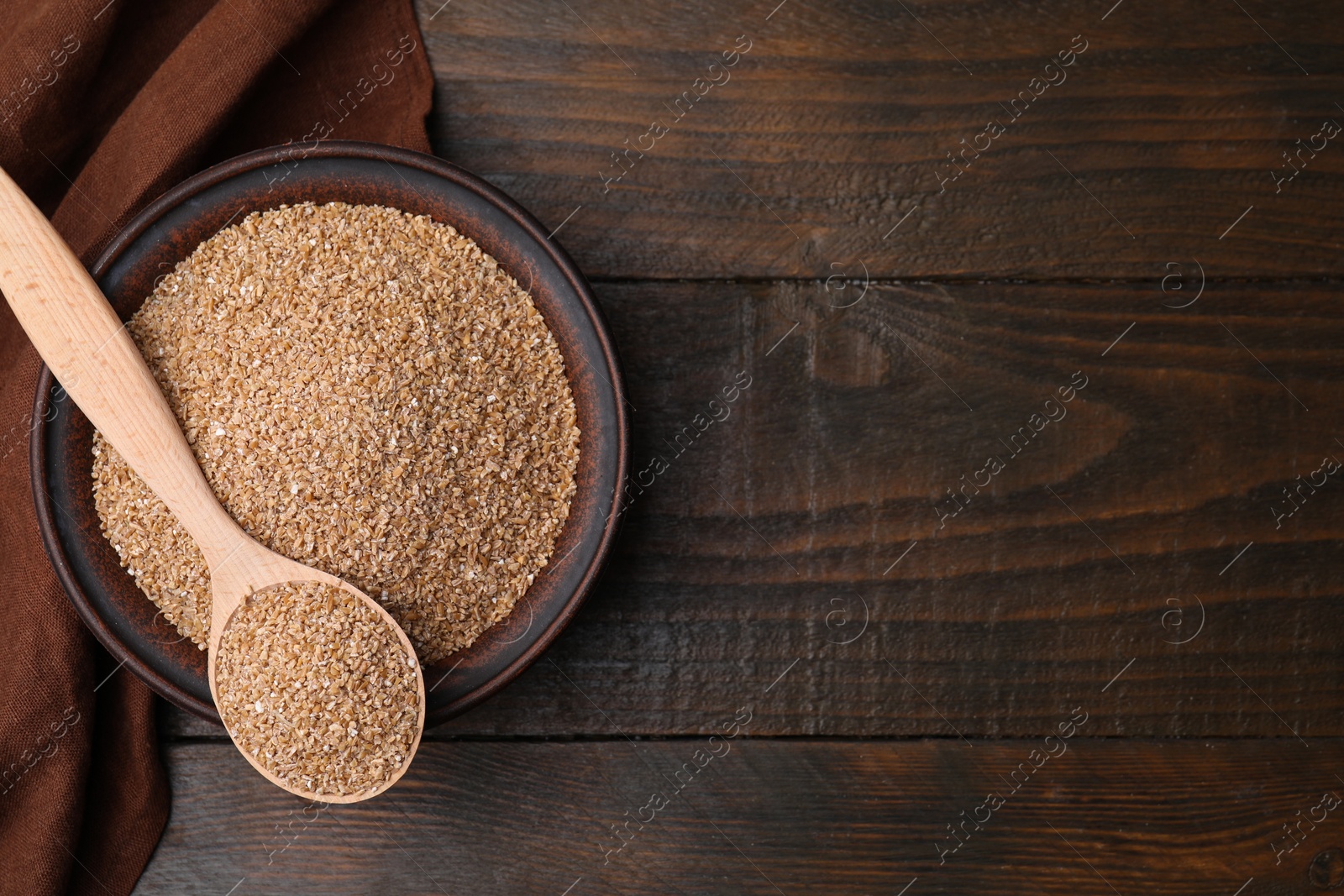 Photo of Dry wheat groats in bowl and spoon on wooden table, top view. Space for text