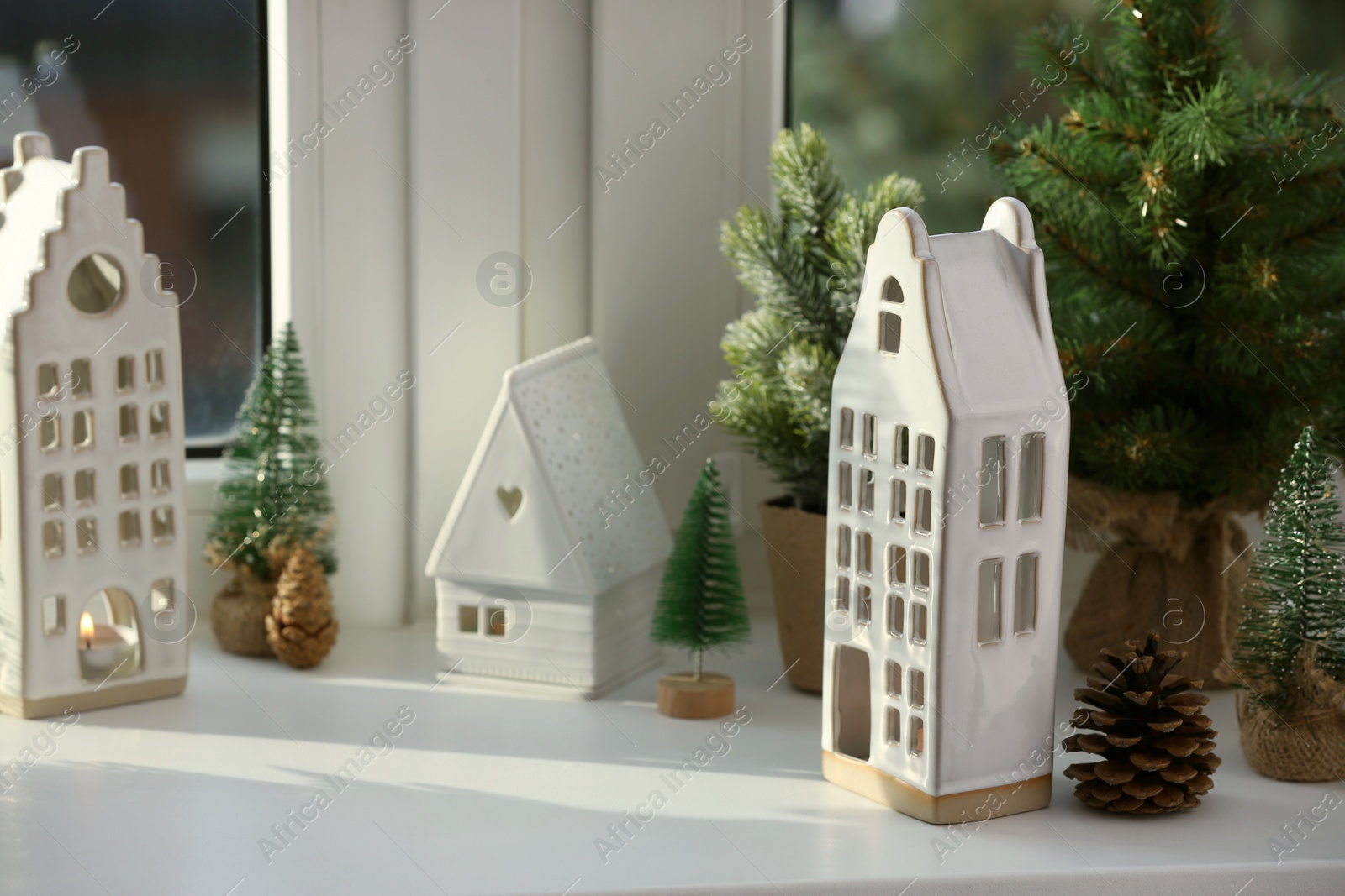 Photo of Beautiful house shaped candle holders and small fir trees on windowsill indoors, space for text