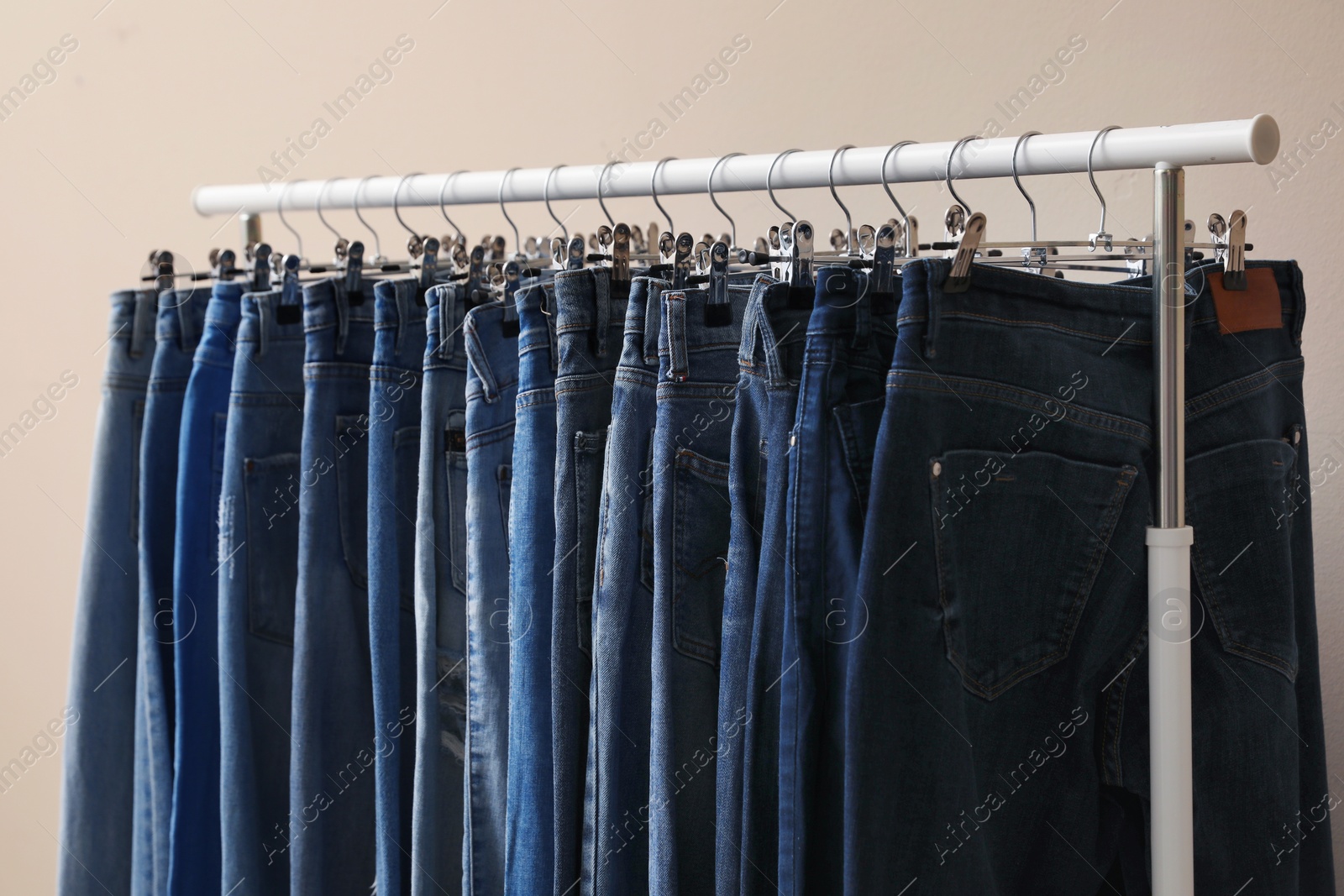 Photo of Rack with stylish jeans on beige background, closeup