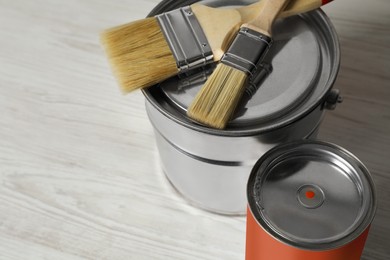 Photo of Can of orange paint, bucket and brushes on white wooden table, closeup. Space for text
