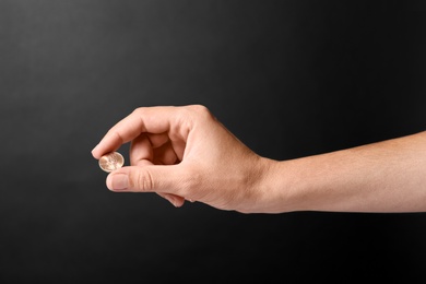 Young woman holding coin on black background, closeup view