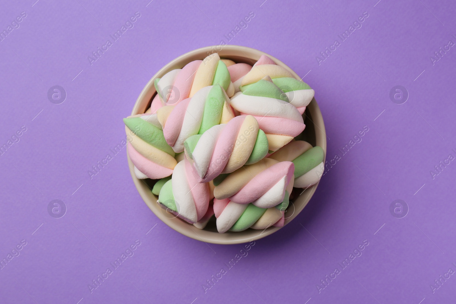 Photo of Delicious colorful marshmallows in bowl on violet background, top view