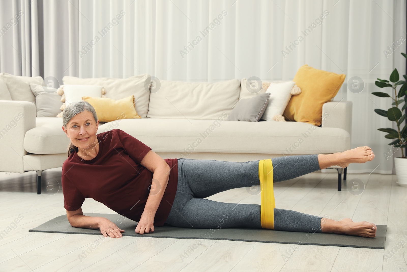 Photo of Senior woman doing exercise with fitness elastic band on mat at home