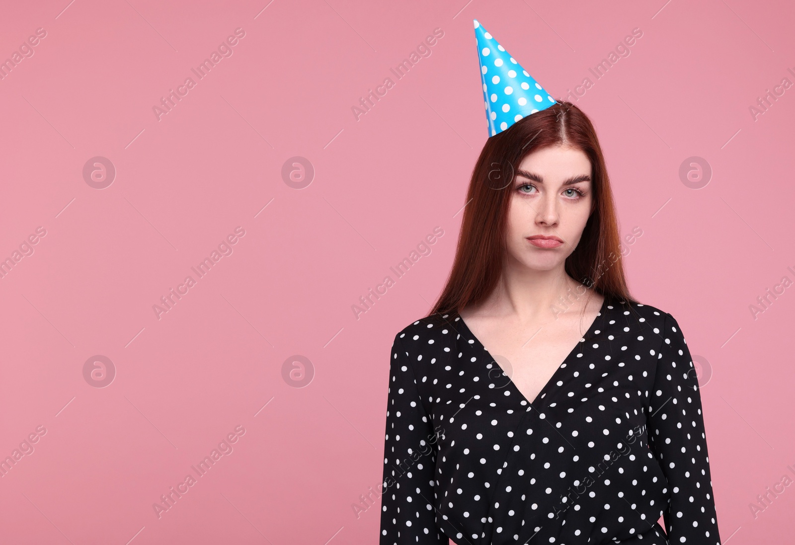 Photo of Sad woman in party hat on pink background, space for text