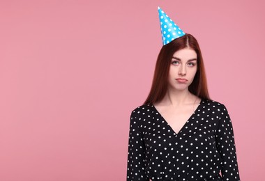 Sad woman in party hat on pink background, space for text