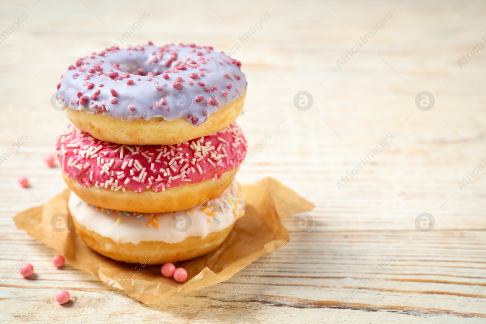 Photo of Delicious glazed donuts on white wooden table. Space for text