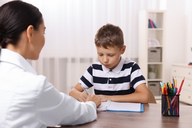 Photo of Dyslexia treatment. Teacher working with boy at table in room