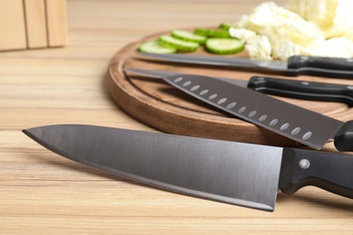 Photo of Set of knives and fresh raw vegetables on wooden table. Clean dishes