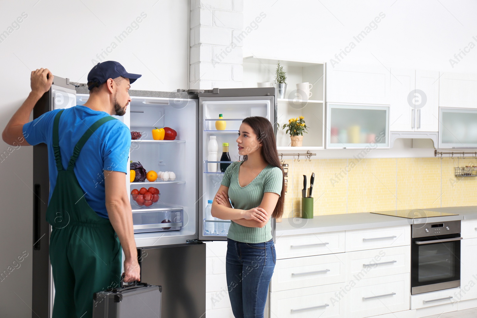 Photo of Male technician talking with client near refrigerator in kitchen