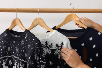 Photo of Woman picking Christmas sweater from rack near white wall, closeup
