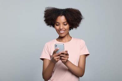 Photo of Smiling African American woman with smartphone on light grey background