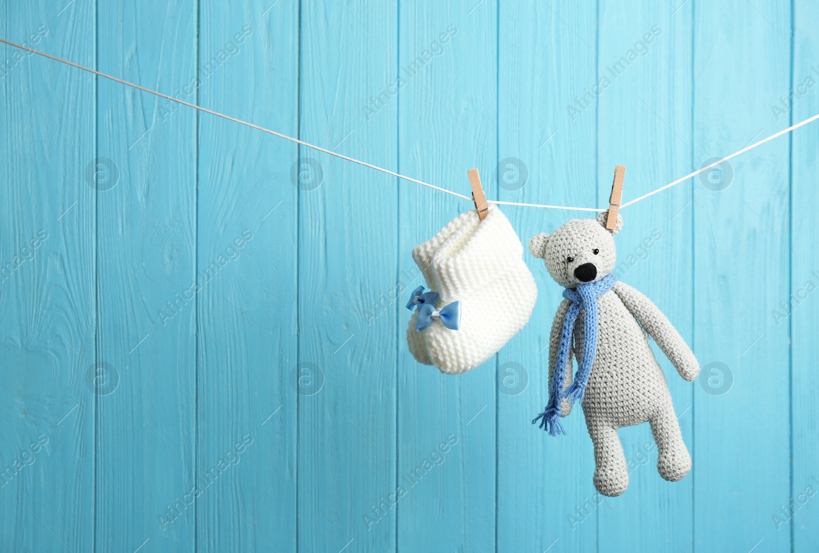 Photo of Baby booties and toy bear on laundry line against color wooden background, space for text. Child accessories