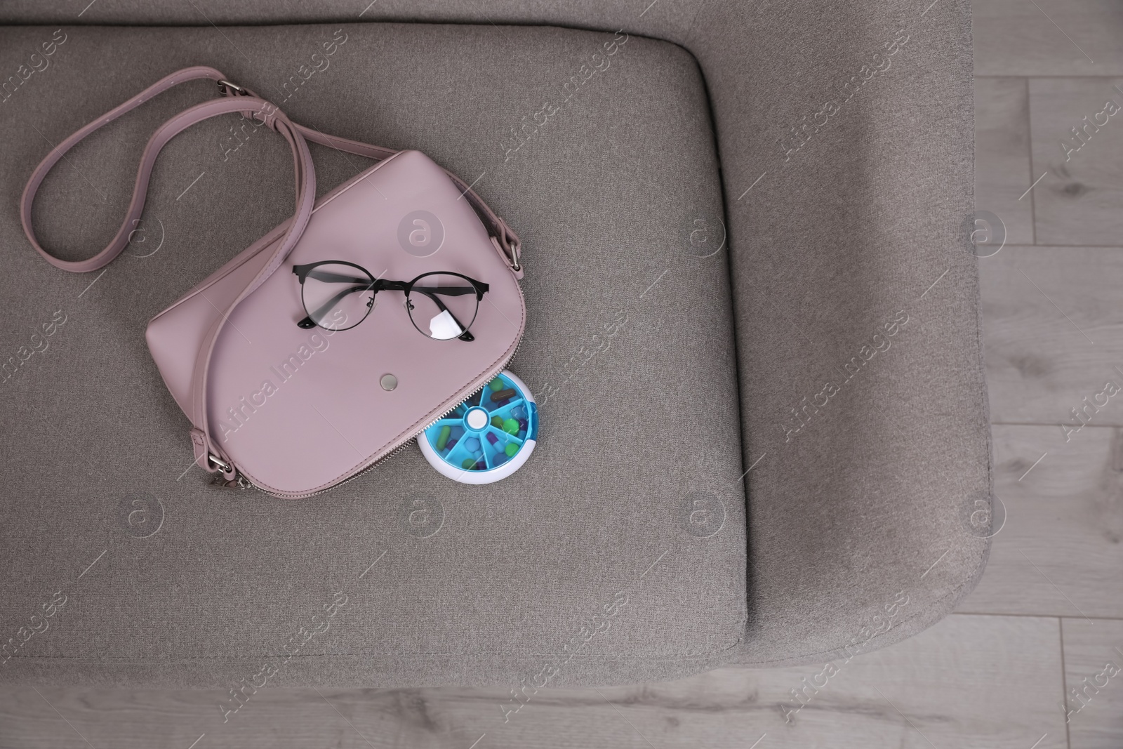 Photo of Pill box with medicaments and glasses near stylish women's bag on sofa indoors, top view. Space for text