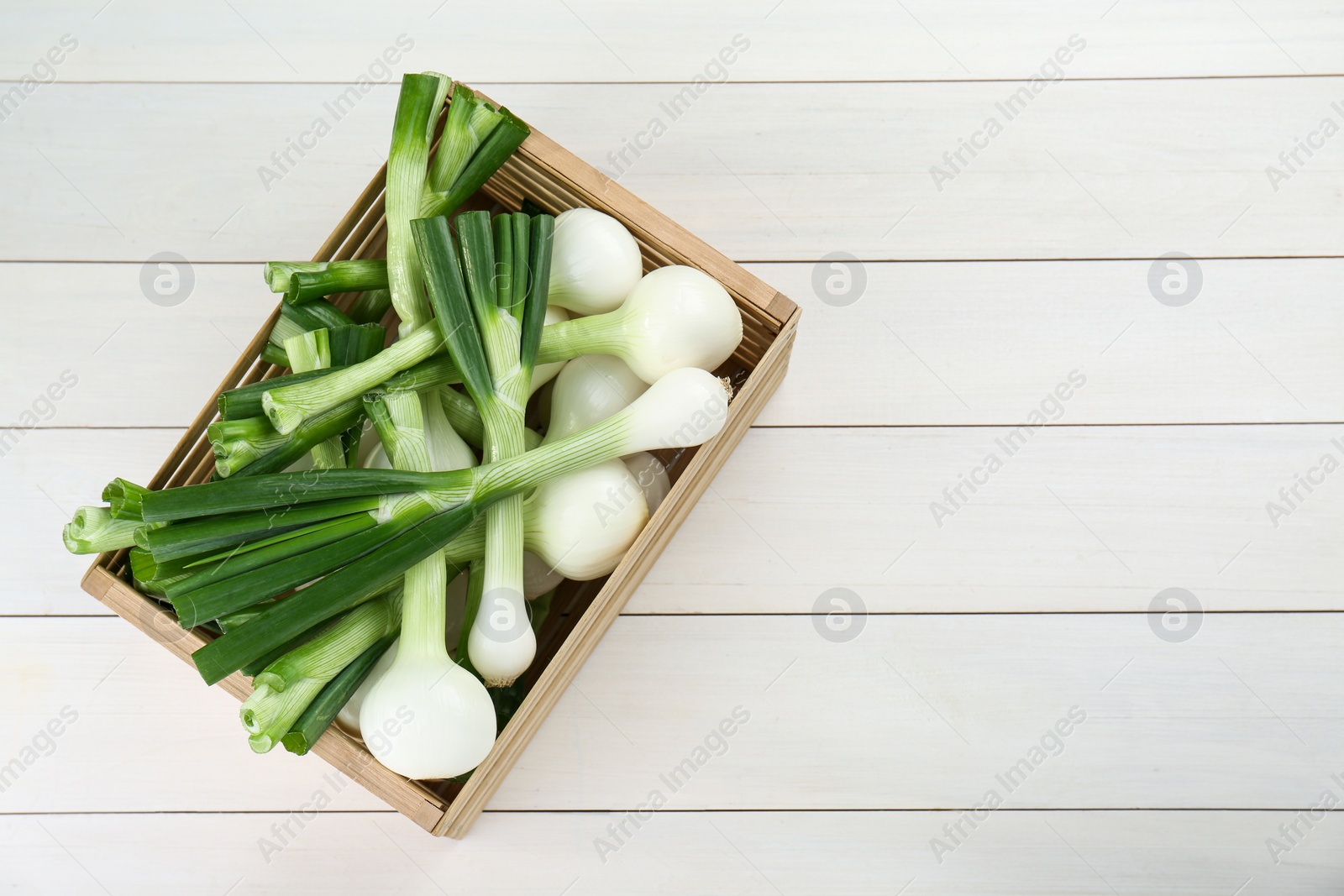 Photo of Crate with green spring onions on white wooden table, top view. Space for text