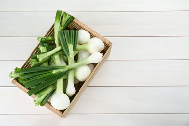 Crate with green spring onions on white wooden table, top view. Space for text