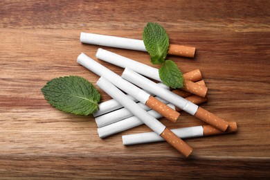 Photo of Menthol cigarettes and mint leaves on wooden table, flat lay