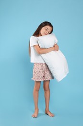 Photo of Cute girl wearing pajamas with pillow on light blue background