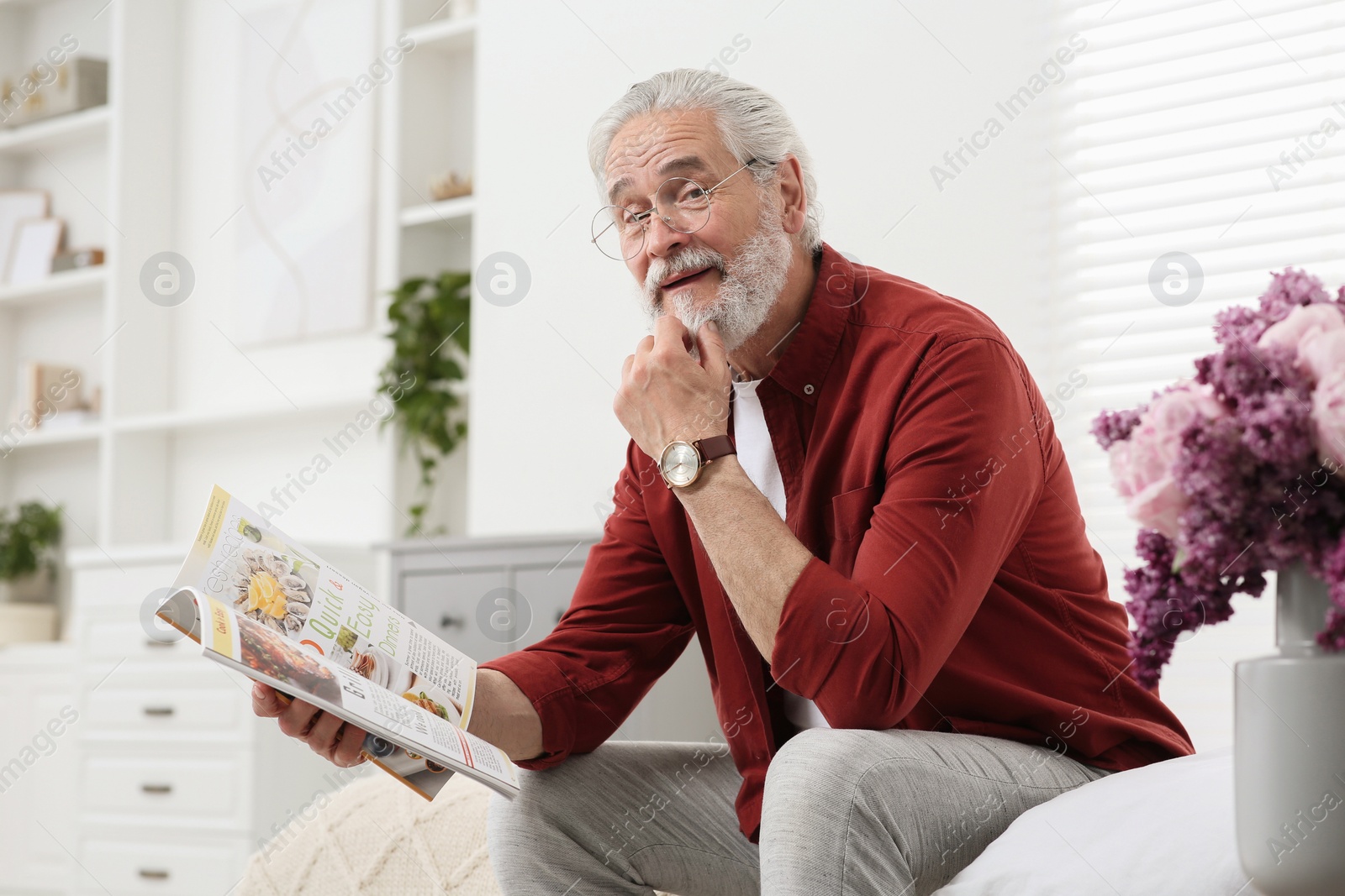 Photo of Senior man in eyeglasses reading magazine on bed at home