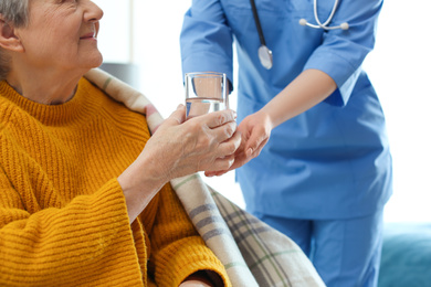 Care worker giving water to elderly woman in geriatric hospice, closeup