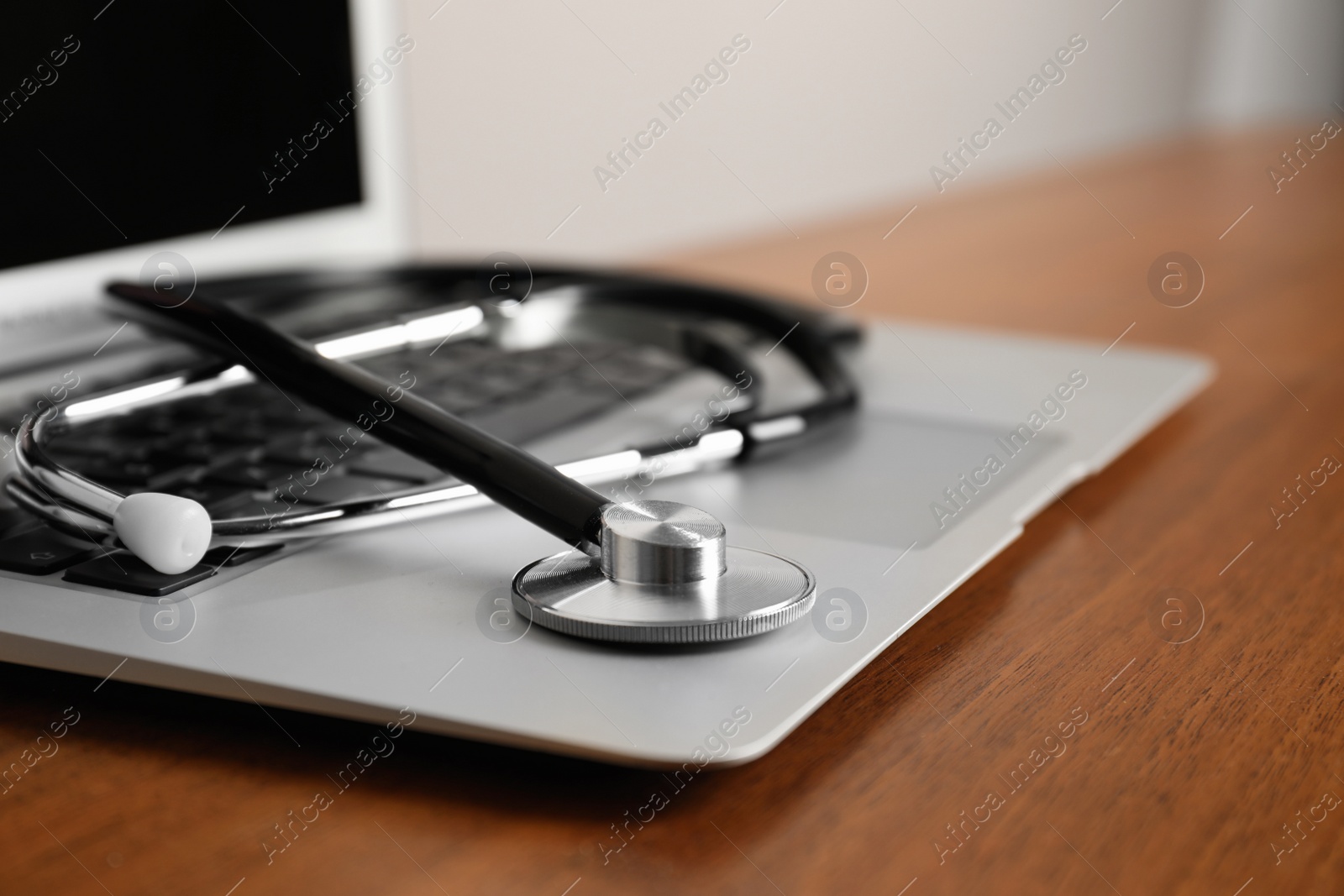 Photo of Modern laptop with stethoscope on wooden table, closeup. Space for text