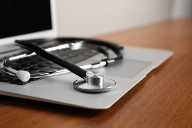 Modern laptop with stethoscope on wooden table, closeup. Space for text