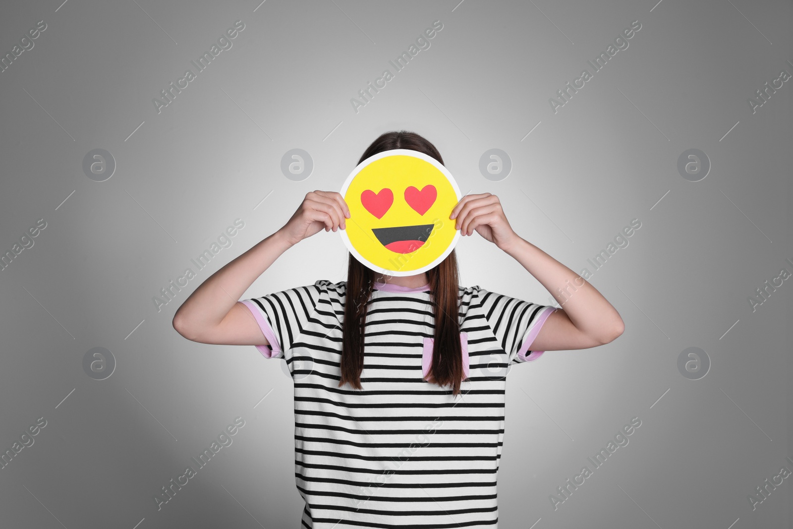 Photo of Woman covering face with heart eyes emoji on grey background